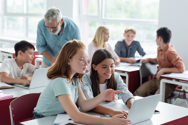 Schulkind zeigt auf Laptop in der Nähe von Lehrer und multiethnischen Klassenkameraden  - Foto, Bild