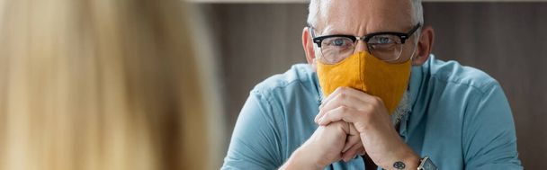 Зрелый учитель в защитной маске смотрит на размытый зрачок, баннер  - Фото, изображение