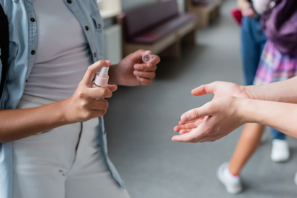 cropped view of teenage schoolgirl spraying hand sanitizer on hands of classmate - Photo, Image