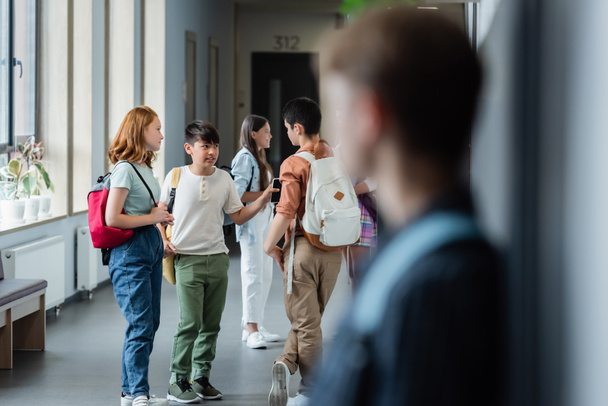 blurred boy standing alone near classmates talking in school corridor - Photo, Image