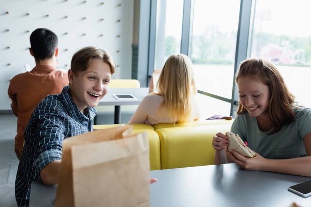 έφηβοι μαθητές χαμογελώντας κατά τη διάρκεια του διαλείμματος στο εστιατόριο του σχολείου - Φωτογραφία, εικόνα