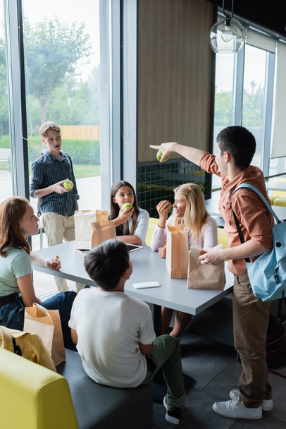 10代の女の子が食堂で昼食をとる生徒の近くで同級生を指差して - 写真・画像