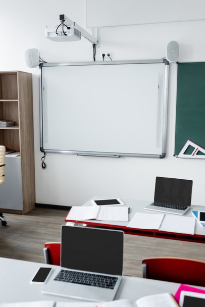 aula moderna con tablero de borrado en la pared y dispositivos digitales en escritorios - Foto, imagen