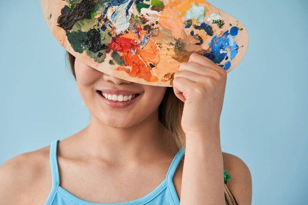 Žena skrývá svůj obličej za paletou s barvami při natáčení ve studiu - Fotografie, Obrázek