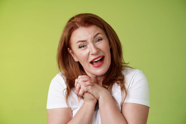 Close-yp touched tender kind redhead middle-aged granny sighing look admiration delight clasp hands heartwarming lovely scene smiling tilting head impressed satisfied stand green background - Foto, afbeelding