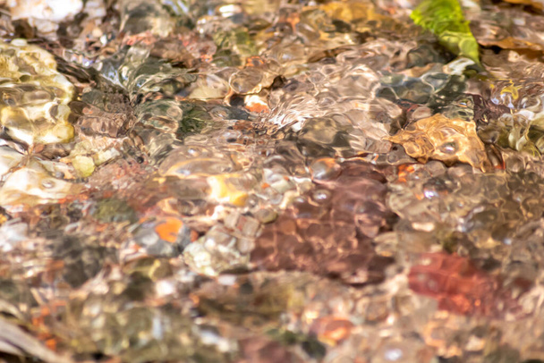 Kövek szikrázó vízben, napsütötte tükröződések a kristálytiszta víz patak vizében, mivel az idilli természeti háttér zen meditációt, kis hullámokat és selymes hullámokat mutat egy egészséges hegyi forrásban - Fotó, kép