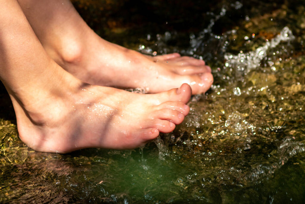 Fiatal fiú játszik mezítláb tiszta vízzel egy kis patak használja a lábát, és a víz forrás lehűti a lábujját és a lábát, és frissíti a tiszta elixír az élet zen meditációs légkörben - Fotó, kép