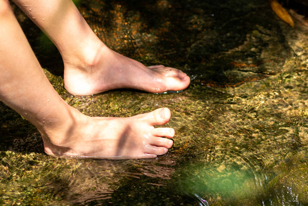 Küçük bir derede çıplak ayakla temiz suyla oynayan genç bir çocuk ayaklarını ve su kaynağını kullanarak ayak parmaklarını ve bacaklarını serinletiyor ve zen meditasyon atmosferindeki saf yaşam iksiriyle ferahlatıyor. - Fotoğraf, Görsel