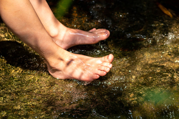 Jongetje blootsvoets spelen met helder water bij een kleine kreek met behulp van zijn voeten en de waterbron koelen zijn tenen en benen en verfrissend met het zuivere elixer van het leven in zen meditatie sfeer - Foto, afbeelding