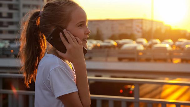 Écolière parle sur smartphone avec concentration au coucher du soleil - Photo, image