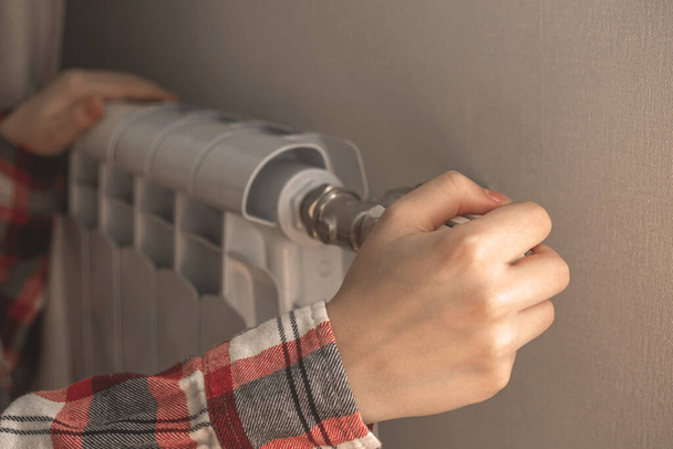 Woman hand adjusting radiator thermostat at home, using a regulator at winter background photo - Foto, afbeelding