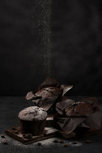 Muffins de chocolate doce frescos polvilhados com açúcar em pó em um fundo preto. Chave baixa. Posição vertical. - Foto, Imagem