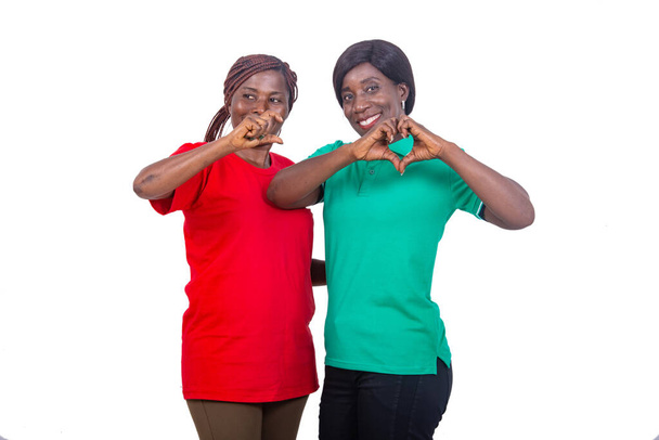 deux femmes mûres gesticulant d'une main. Femme en T-shirt vert faisant une forme de coeur avec ses mains et l'autre faisant un geste "C" avec sa main. - Photo, image