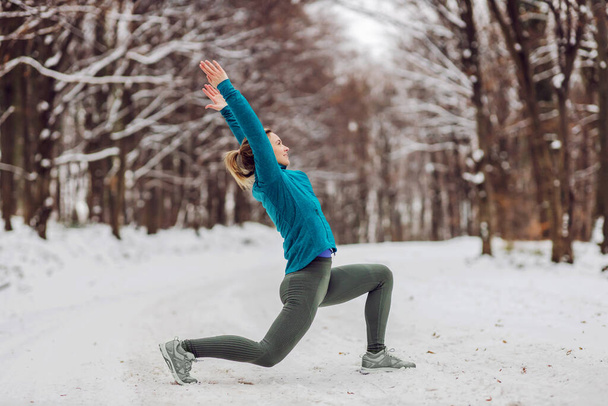 Sportlerin im warmen Outfit bei Yoga-Übungen im verschneiten Wald. Fitness im Freien, Schnee, Kälte, Winteryoga - Foto, Bild