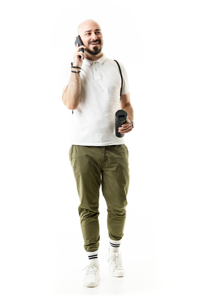 Счастливый расслабленный ботаник в хипстерском стиле молодой человек ходит и разговаривает по телефону. Портрет полностью изолирован на белом фоне - Фото, изображение