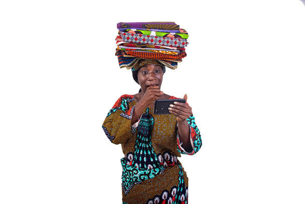 γυναίκα με παραδοσιακά loincloths στο κεφάλι έκπληκτος με το χέρι στο στόμα, ενώ κοιτάζοντας οθόνη του κινητού. - Φωτογραφία, εικόνα