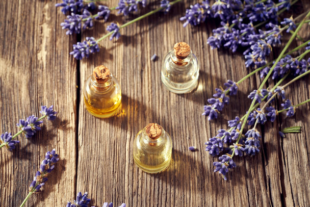 Tres botellas de aceite esencial de aromaterapia con flores frescas de lavanda sobre una mesa de madera - Foto, Imagen