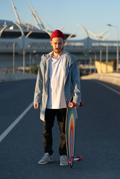 Hipsterski deskorolkarz z longboardem na ulicy. Modna koncepcja miejskiego stylu życia - Zdjęcie, obraz