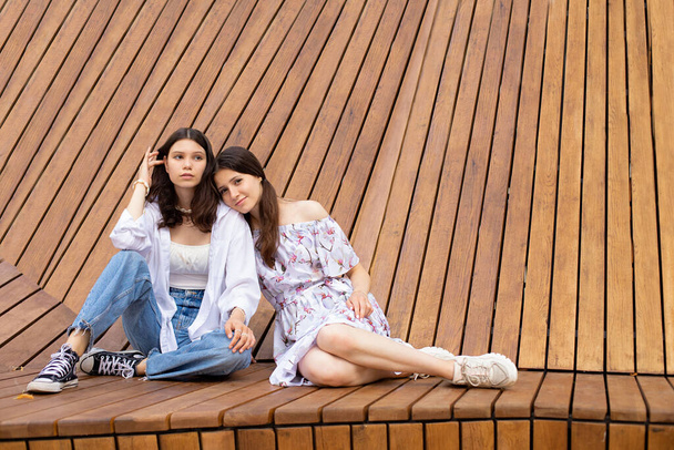 dos hermanas niñas están sentadas en un gran banco de madera al aire libre - Foto, Imagen