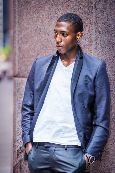 Afrikkalainen amerikkalainen teini-ikäinen poika, yllään musta muodikas takki, valkoinen v niskapaita, seisoo pylvästä vasten kadulla, ajattelematta, ajatuksissaan. - Valokuva, kuva