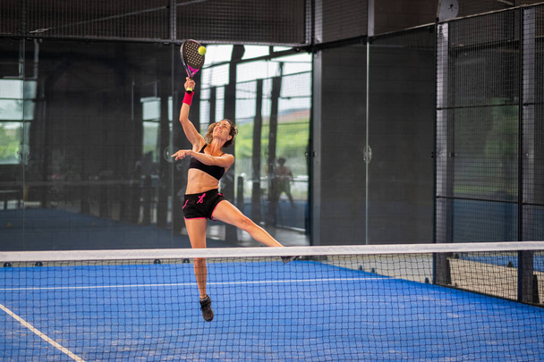 Mujer jugando al padel en una cancha de padel de hierba azul interior - Joven mujer deportista jugador de padel golpeando la pelota con una raqueta - Foto, imagen