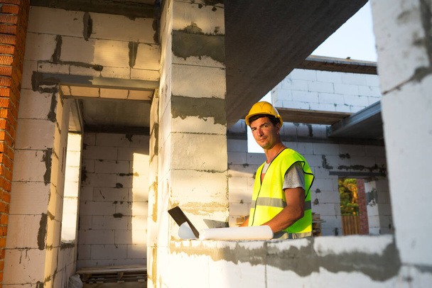 Construction engineer on the construction site of a house made of porous concrete blocks works at a computer in a reflective safety vest and hardhat. Design, construction, drawings project, check - Фото, зображення