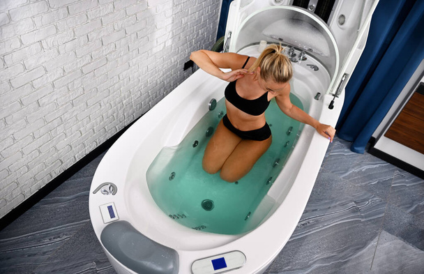 Vista de alto ângulo de uma mulher com corpo perfeito recebendo tratamento de beleza na banheira da cápsula de spa aberta - Foto, Imagem