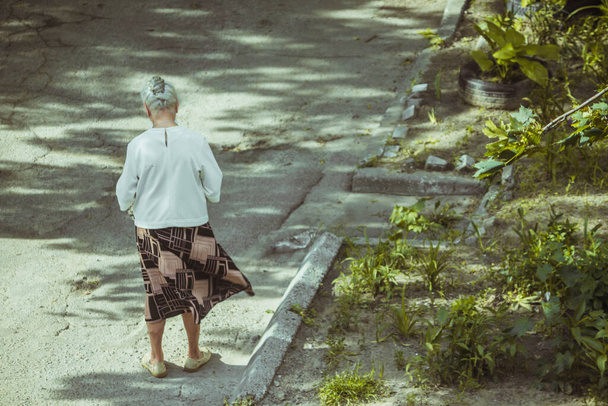 Grandmother with gray hair walks around the yard. - Фото, изображение