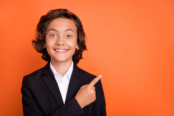 Photo of happy positive cheerful little boy point finger empty space good mood news isolated on orange color background - 写真・画像