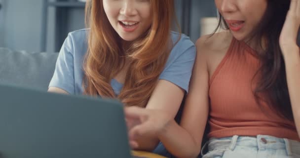 Két ázsiai leszbikus nő a kanapén együtt nézi a laptopot otthon a nappaliban. Boldog pár szobatárs hölgyek élvezik internetes szörfözés online vásárlás, Életmód nő otthon koncepció. - Felvétel, videó
