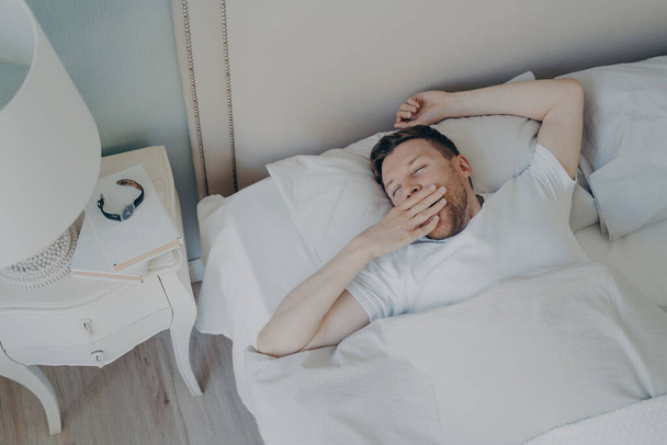 Veselý mladý atraktivní muž se ráno probudí v posteli - Fotografie, Obrázek
