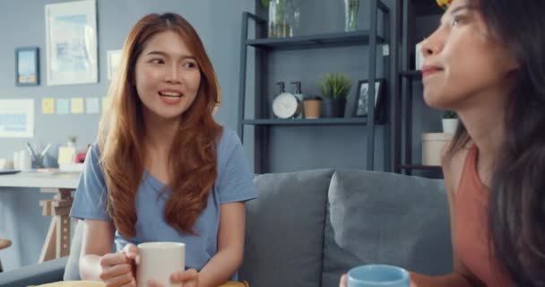 Asia housewife women with casual relax on couch with cup of tea talk together about their life and husband relationship gossip in living room at house. Girls friends roommate stay in dorm together. - Footage, Video