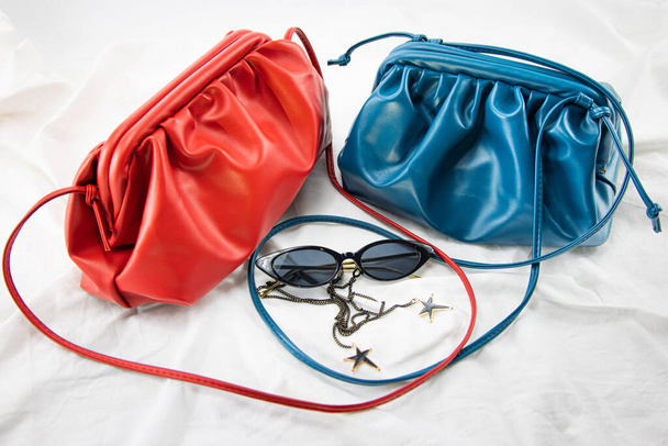Жіноча сумка з чорними сонцезахисними окулярами на білому тлі. Шкіряна сумка на зібраній тканині. Бічна концепція моди вишуканих модних окулярів та розкішної справжньої шкіряної сумочки
 - Фото, зображення