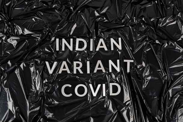 palabras indio variante covid establecido con letras de metal de plata sobre arrugado negro bolsa de plástico de fondo - Foto, Imagen
