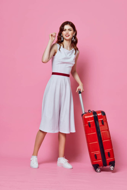 woman with red suitcase white dress emotions travel pink background - Foto, afbeelding