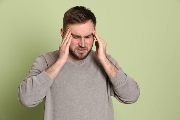 Man suffering from migraine on light green background - Foto, imagen