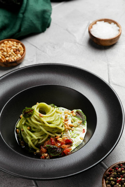 green pasta spaghetti with pesto sauce, tomatoes and basil. Pasta with spinach roasted vegetables and nuts. - Foto, Imagen