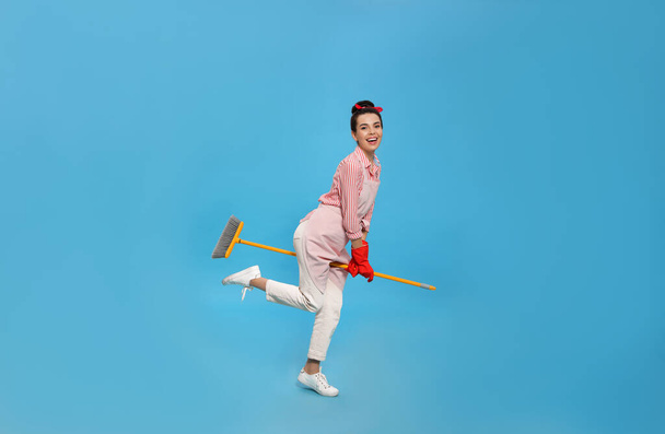 Young housewife with broom having fun on light blue background - Foto, immagini