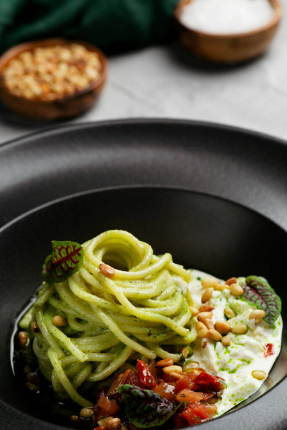 green pasta spaghetti with pesto sauce, tomatoes and basil. Pasta with spinach roasted vegetables and nuts. - Foto, Imagem