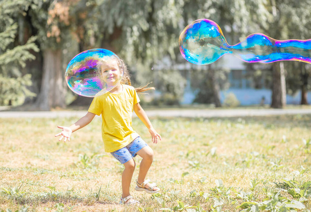 Mutlu bir kız büyük sabun köpükleri yakalar, bir çocuk sokakta oynar, havada hafif balonlar süzülür.. - Fotoğraf, Görsel