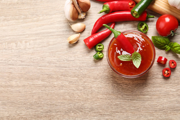 Spicy chili sauce and ingredients on wooden table, flat lay. Space for text - 写真・画像