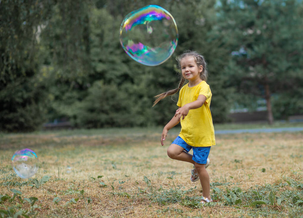 Una chica feliz atrapa grandes burbujas de jabón, un niño juega en la calle, globos de luz se elevan en el aire. - Foto, Imagen