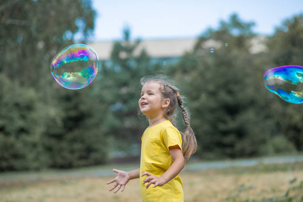 Ein glückliches Mädchen fängt große Seifenblasen, ein Kind spielt auf der Straße, Lichtballons steigen in die Luft. - Foto, Bild