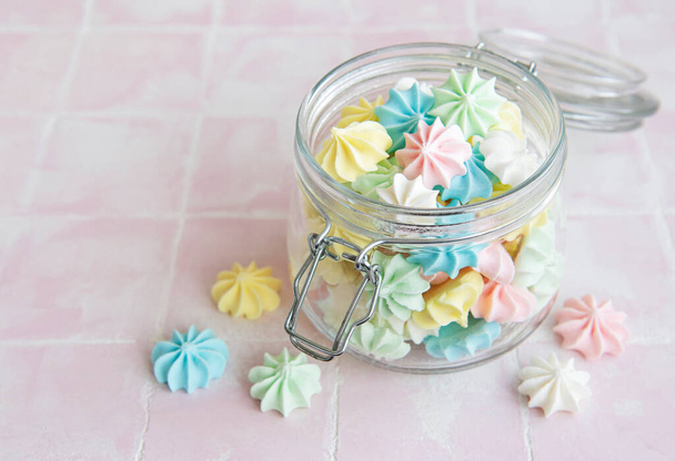 Small colorful meringues in the  glass jar on pink tile background - Photo, Image