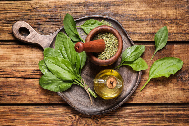 Fresh and dried broadleaf plantain leaves with essential oil on wooden table, flat lay - Φωτογραφία, εικόνα