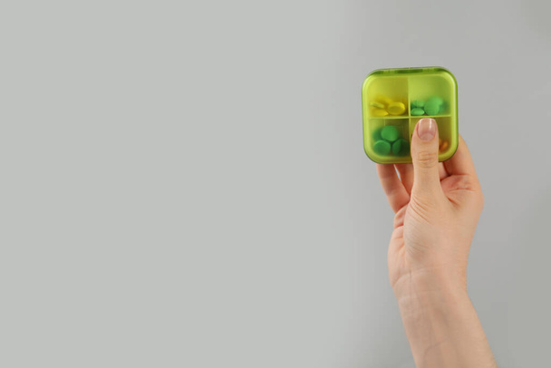 Woman holding plastic box with different pills on light grey background, closeup. Space for text - 写真・画像