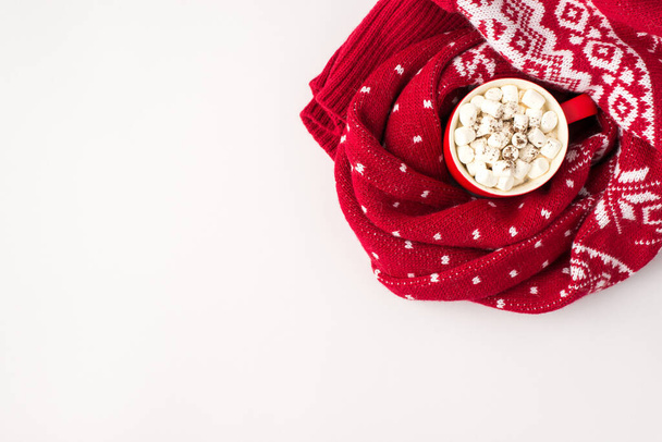 Bovenaanzicht foto van rode beker warm drinken met marshmallow verpakt in rode trui met ornament op geïsoleerde witte achtergrond met copyspace - Foto, afbeelding