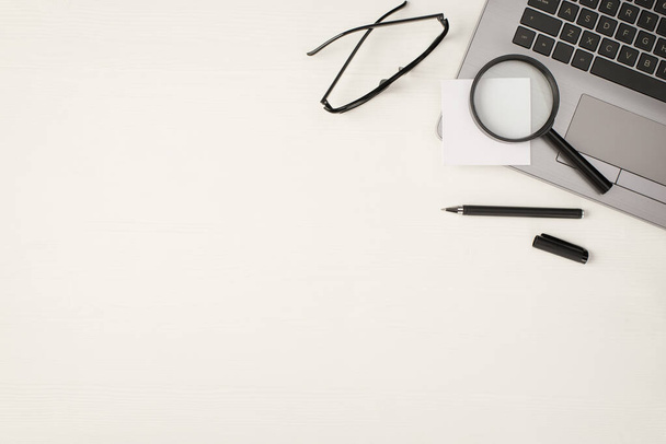 Вид сверху фото увеличительное стекло наклейка бумагу на ноутбуке черная ручка и очки на изолированном белом фоне деревянный стол с пустым пространством - Фото, изображение