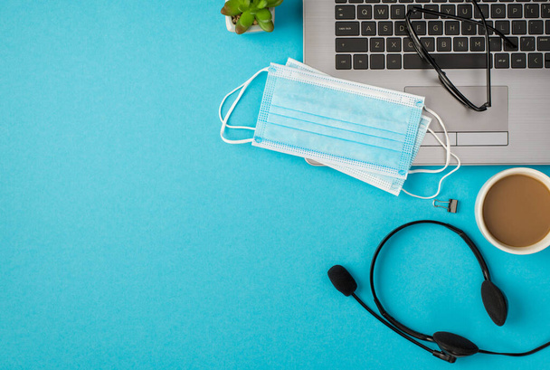 Widok z góry zdjęcie okularów dwie maski medyczne na laptopie segregator słuchawki słuchawki doniczka i filiżanka napoju na odizolowanym pastelowym tle niebieski z pustą przestrzenią - Zdjęcie, obraz