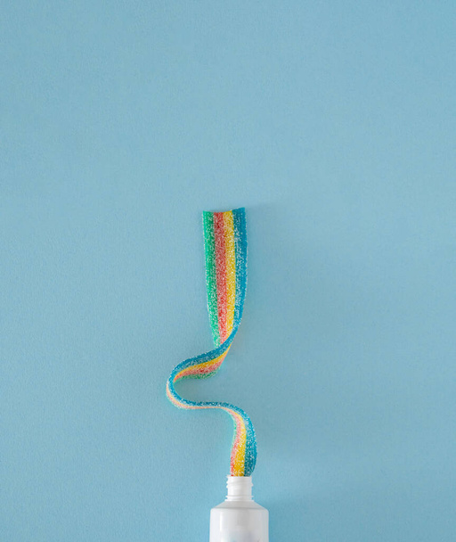 toothpaste with rainbow color on the pastel blue background. abstract art. minimal flat lay with copy space - Фото, изображение